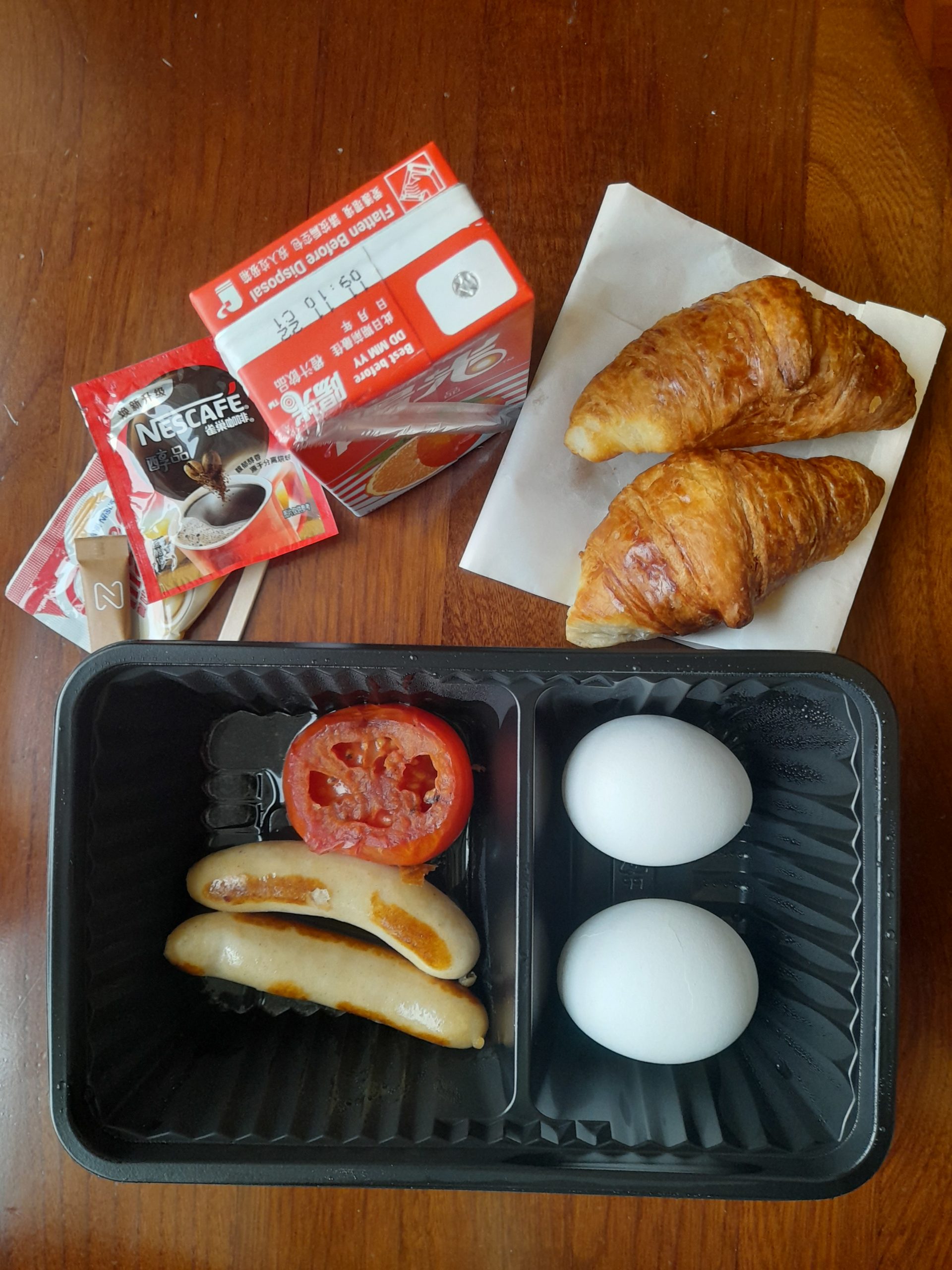 Quarantine breakfast of boiled eggs, sausages, tomato, croissants, and drinks