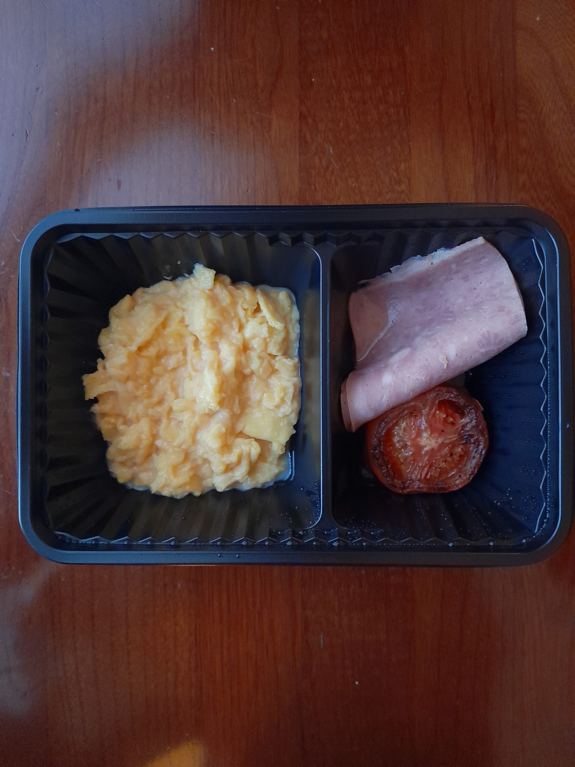 Part of a quarantine breakfast meal with scrambled eggs, ham slices, tomato